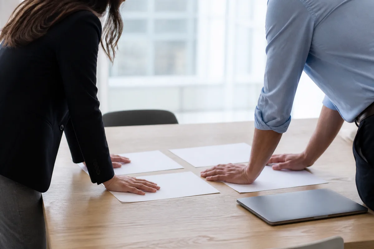 Deux personnes comparant des documents de gestion autour d&rsquo;une table de réunion en bois